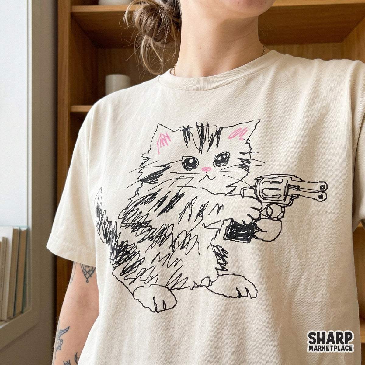 Funny tabby kitten holding a large toy gun, rendered in a raw sketch aesthetic, displayed as a graphic print on a beige t-shirt for apparel design.