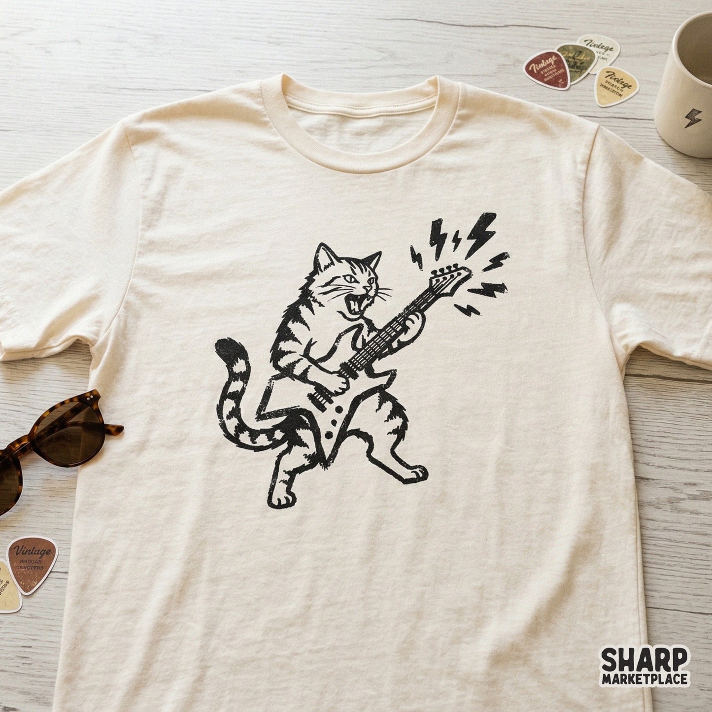 Distressed black ink design of a tabby cat playing an electric guitar, printed on a cream colored t-shirt for a trendy apparel look.
