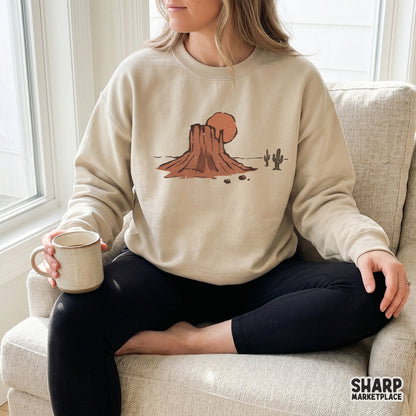 Retro southwestern desert landscape design with a mesa and cacti, shown printed on a beige crewneck sweatshirt for a boho apparel look.