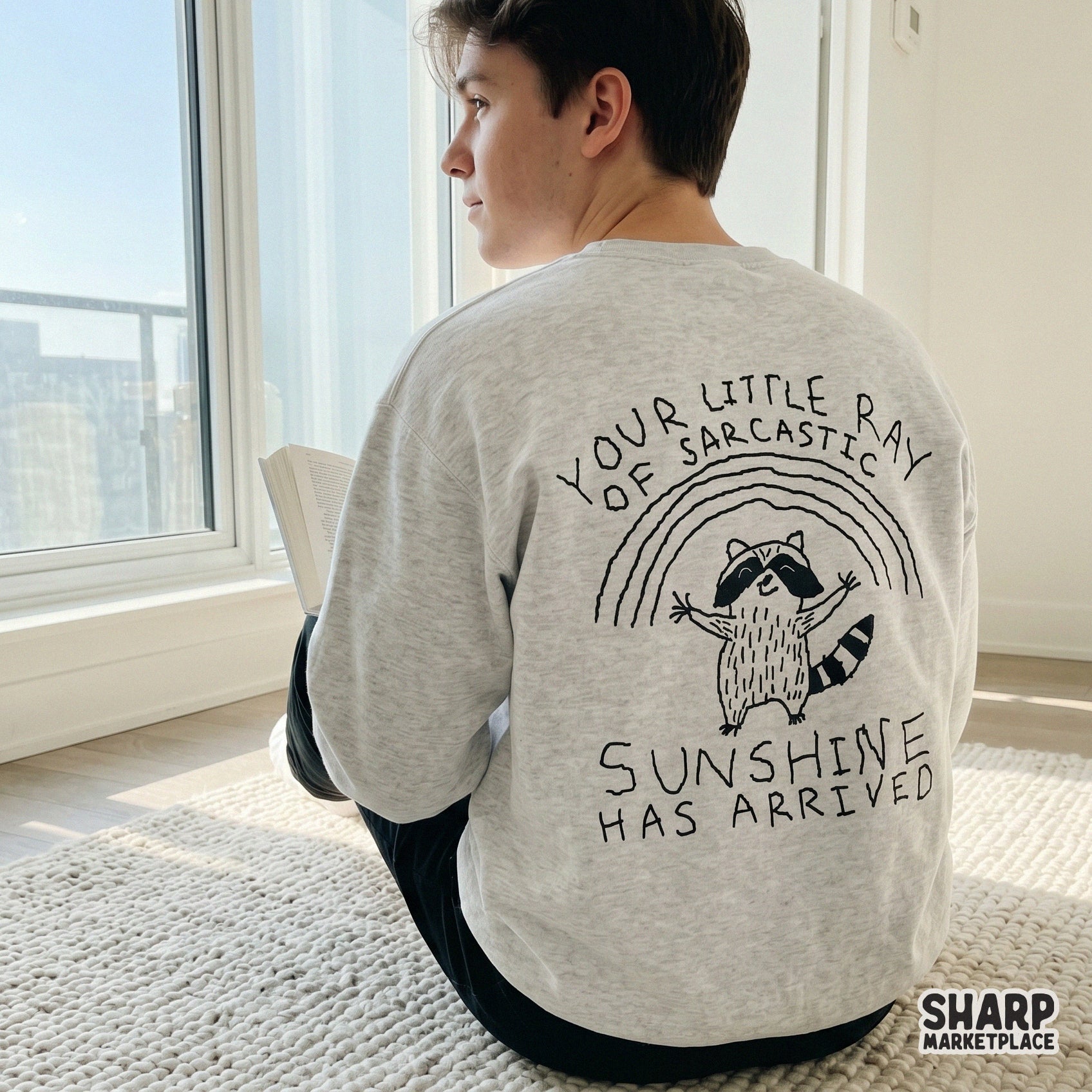 Hand-drawn style raccoon graphic with a rainbow and sarcastic sunshine quote for trendy print-on-demand apparel and craft projects.