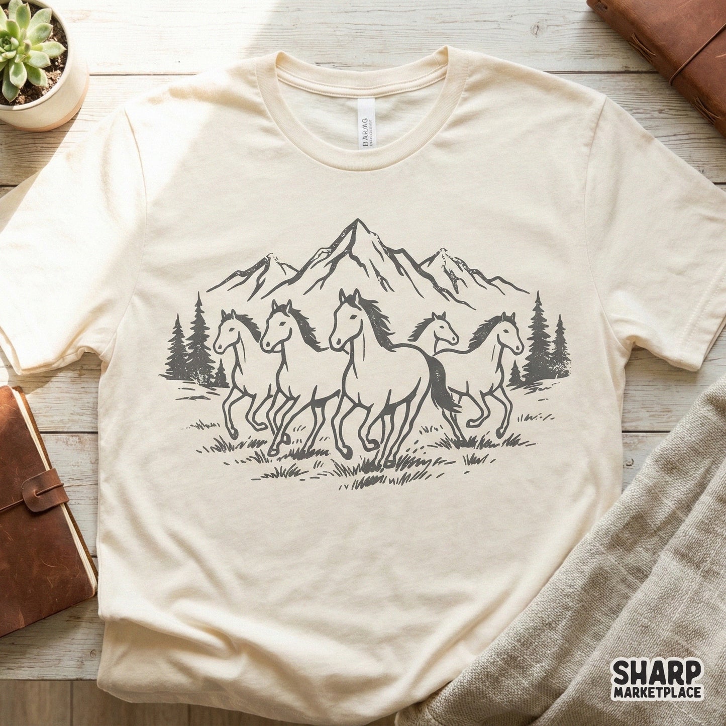 Cream colored t-shirt featuring a monochromatic charcoal illustration of wild horses running through a mountain forest for western apparel.