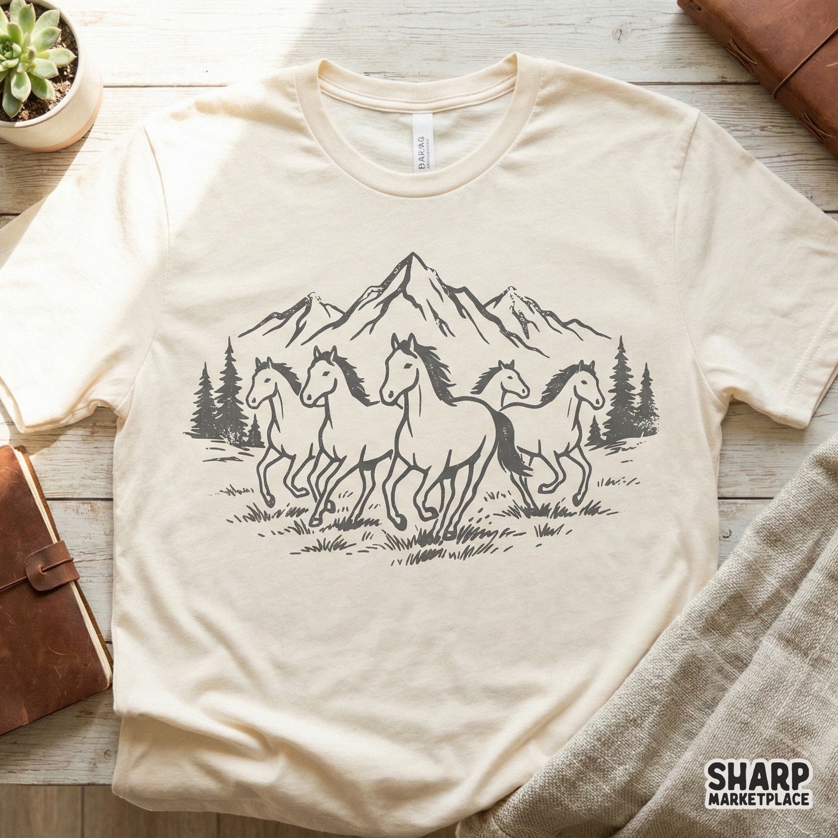 Cream colored t-shirt featuring a monochromatic charcoal illustration of wild horses running through a mountain forest for western apparel.