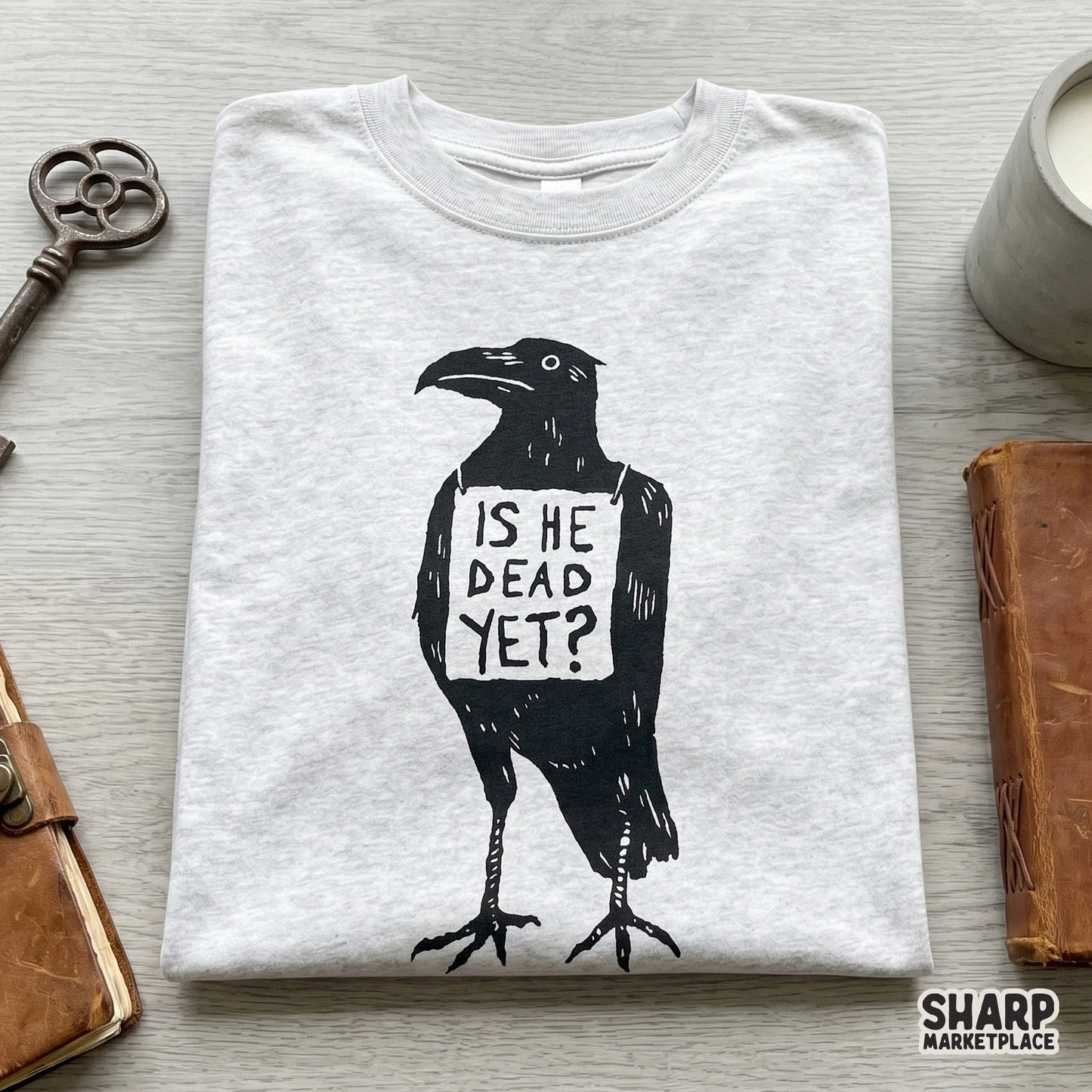 Minimalist black raven silhouette holding a protest sign with the text Is He Dead Yet, ideal for gothic stickers, tumblers, and dark humor apparel.
