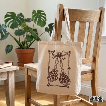 Tote bag mockup featuring a brown line art design of two checkered skulls hanging from a ribbon bow within a star-bordered frame.