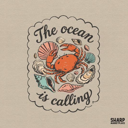 Retro coastal design featuring an orange crab surrounded by seashells and the text The Ocean Is Calling inside a scalloped border for summer apparel.