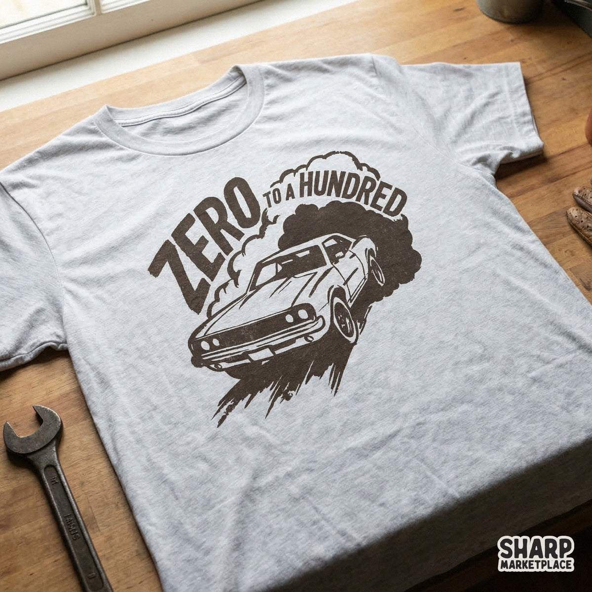 Distressed black and white muscle car design with smoke and Zero To A Hundred text, shown printed on a light gray t-shirt for apparel.