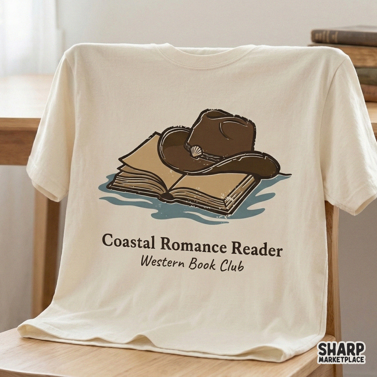 Trendy western beach book club digital design printed on a cream t-shirt, showing a cowboy hat resting on an open book with vintage typography.