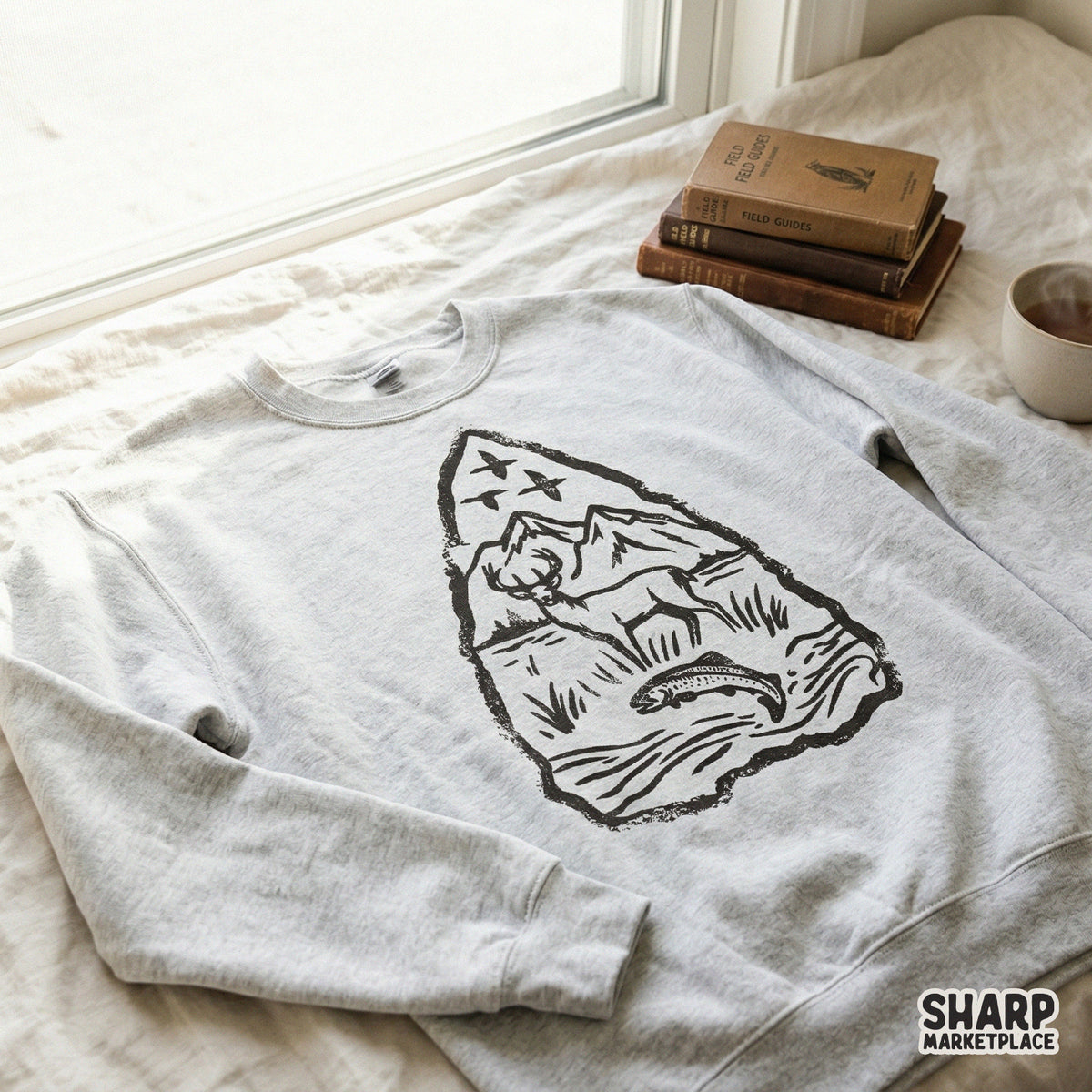 Vintage-style arrowhead graphic with a deer, fish, and mountains, displayed on a grey sweatshirt for a trendy outdoor aesthetic.
