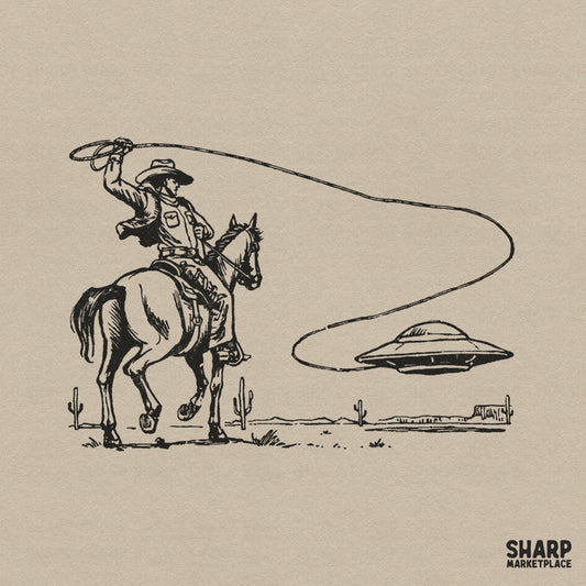 Vintage black ink sketch of a cowboy on horseback lassoing a flying saucer in a desert landscape with cacti for western apparel sublimation.