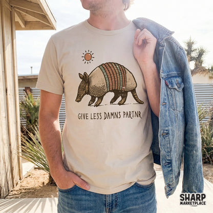 Trendy western apparel design featuring a walking armadillo, a simple orange sun, and sarcastic handwritten text on a light-colored shirt.