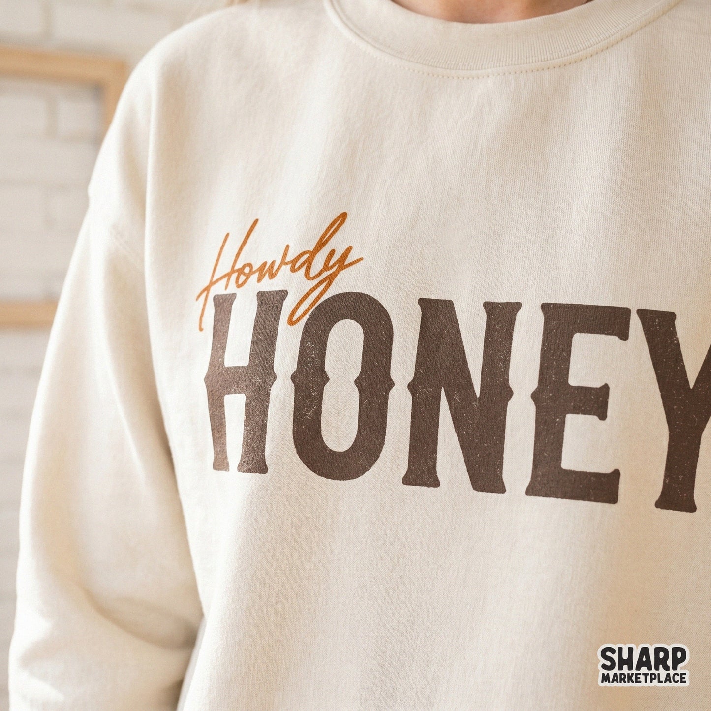 Western style Howdy Honey sublimation graphic displayed on a cream-colored sweatshirt, showcasing rustic brown and orange typography.