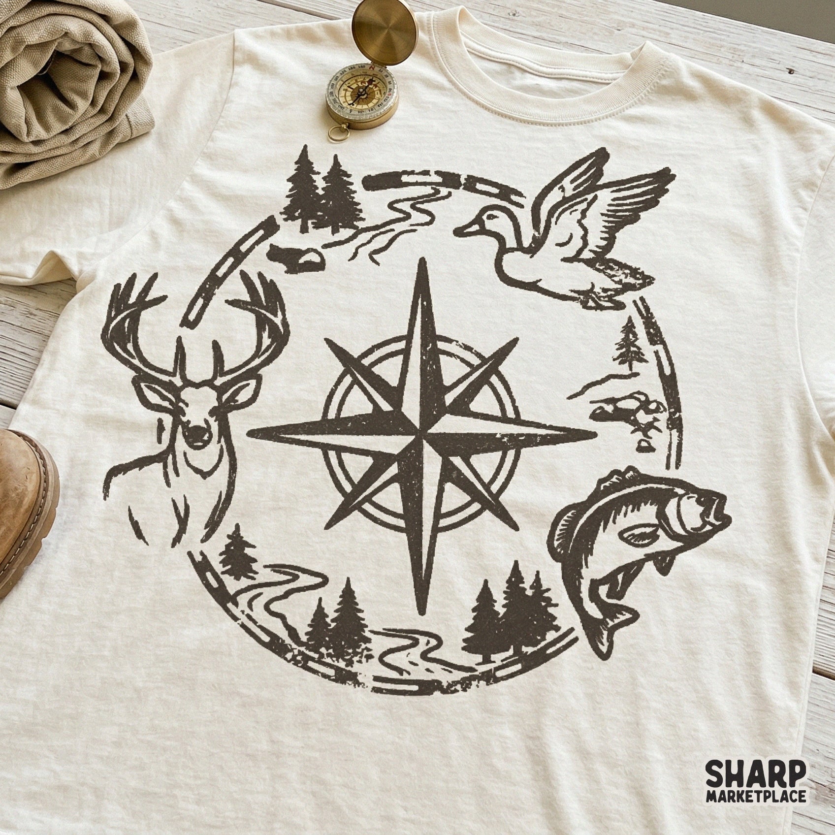 Outdoor lodge emblem digital graphic on a t-shirt mockup, showcasing a compass rose surrounded by hunting and fishing wilderness elements.