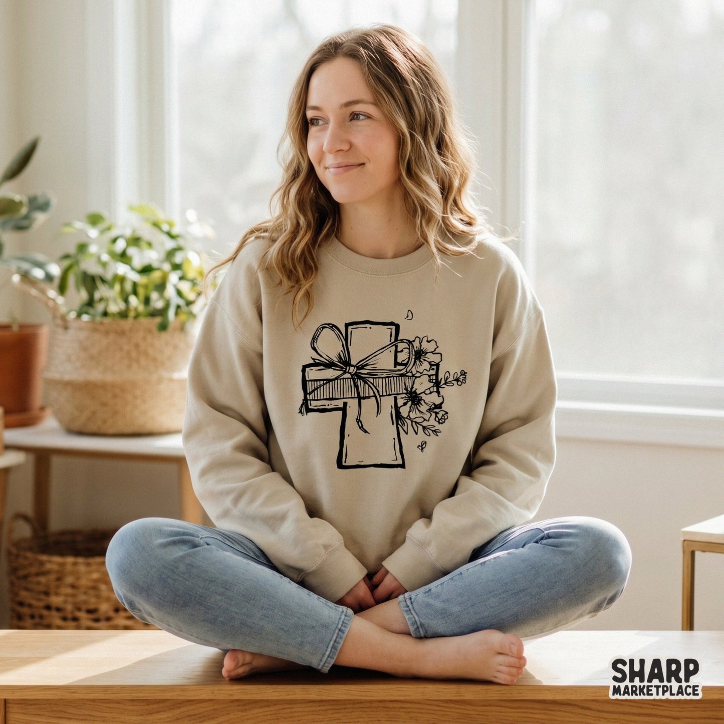 A beige sweatshirt featuring a black line art design of a cross adorned with a ribbon bow and wildflowers, perfect for faith-based apparel.