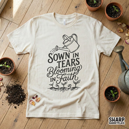 A cream-colored t-shirt mockup displaying a black ink botanical design with the inspirational quote Sown In Tears Blooming In Faith and sprout graphics.