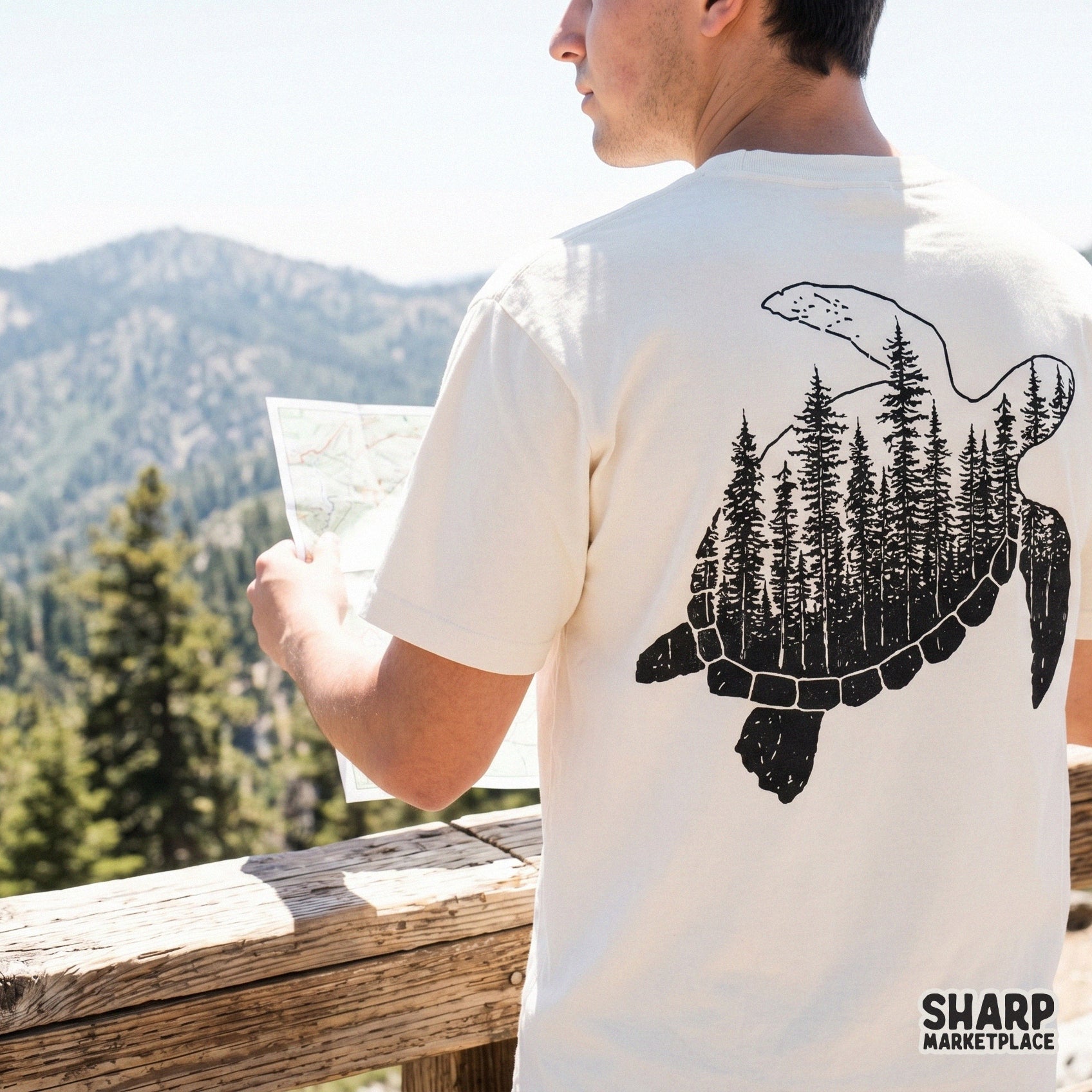 Back view of a person wearing a cream t-shirt featuring a black ink sea turtle design filled with a detailed pine forest silhouette.