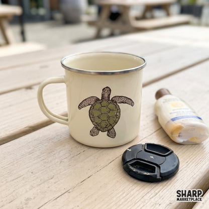 Hand-drawn sea turtle graphic in a rustic woodcut style, displayed on a cream-colored camping mug for a trendy coastal aesthetic.