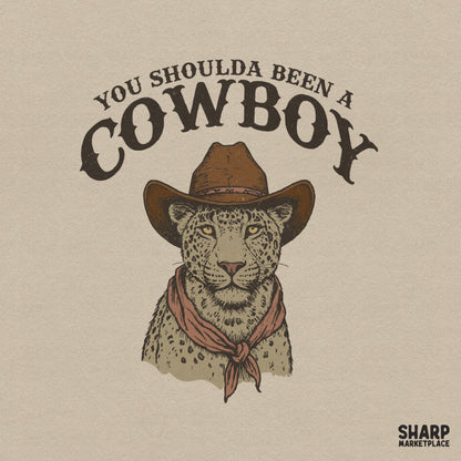 Hand-drawn leopard wearing a brown cowboy hat and red bandana with vintage You Shoulda Been A Cowboy text for sublimation or apparel printing.