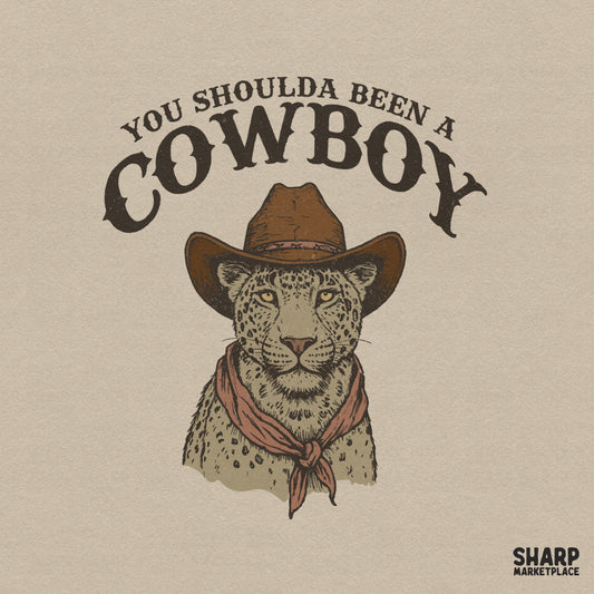 Hand-drawn leopard wearing a brown cowboy hat and red bandana with vintage You Shoulda Been A Cowboy text for sublimation or apparel printing.