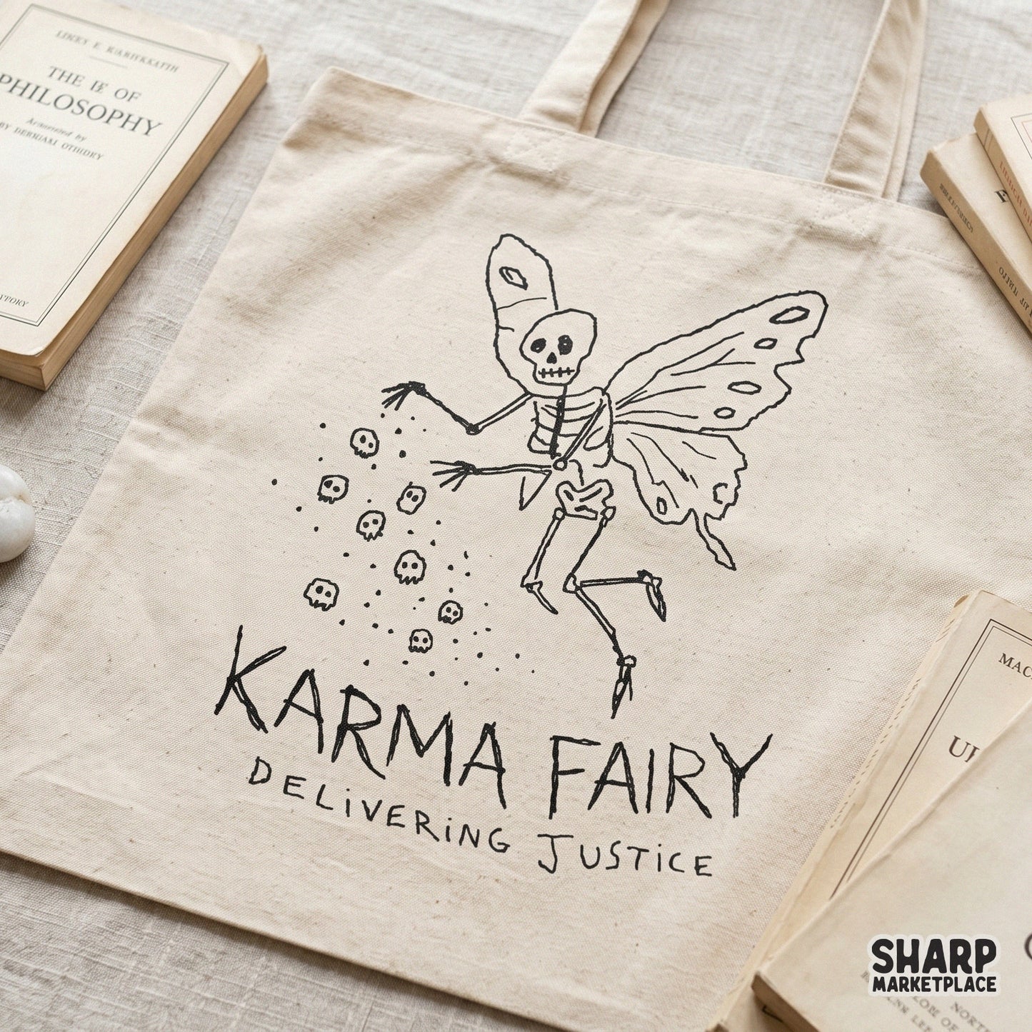Tote bag featuring a black line art design of a skeleton fairy with butterfly wings dropping skulls, with the text Karma Fairy Delivering Justice below.
