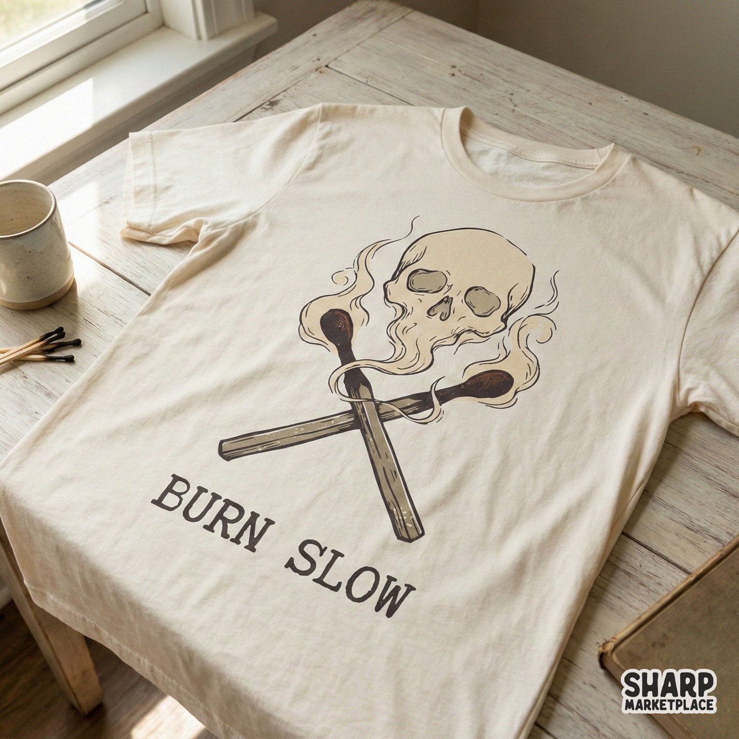 Retro style digital design featuring a skull emerging from smoke above crossed matches with the phrase Burn Slow for custom t-shirt printing.