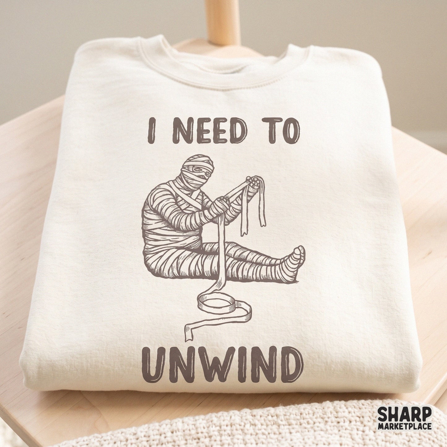 Funny unraveling mummy character with a sarcastic I Need To Unwind quote for retro Halloween shirt sublimation designs