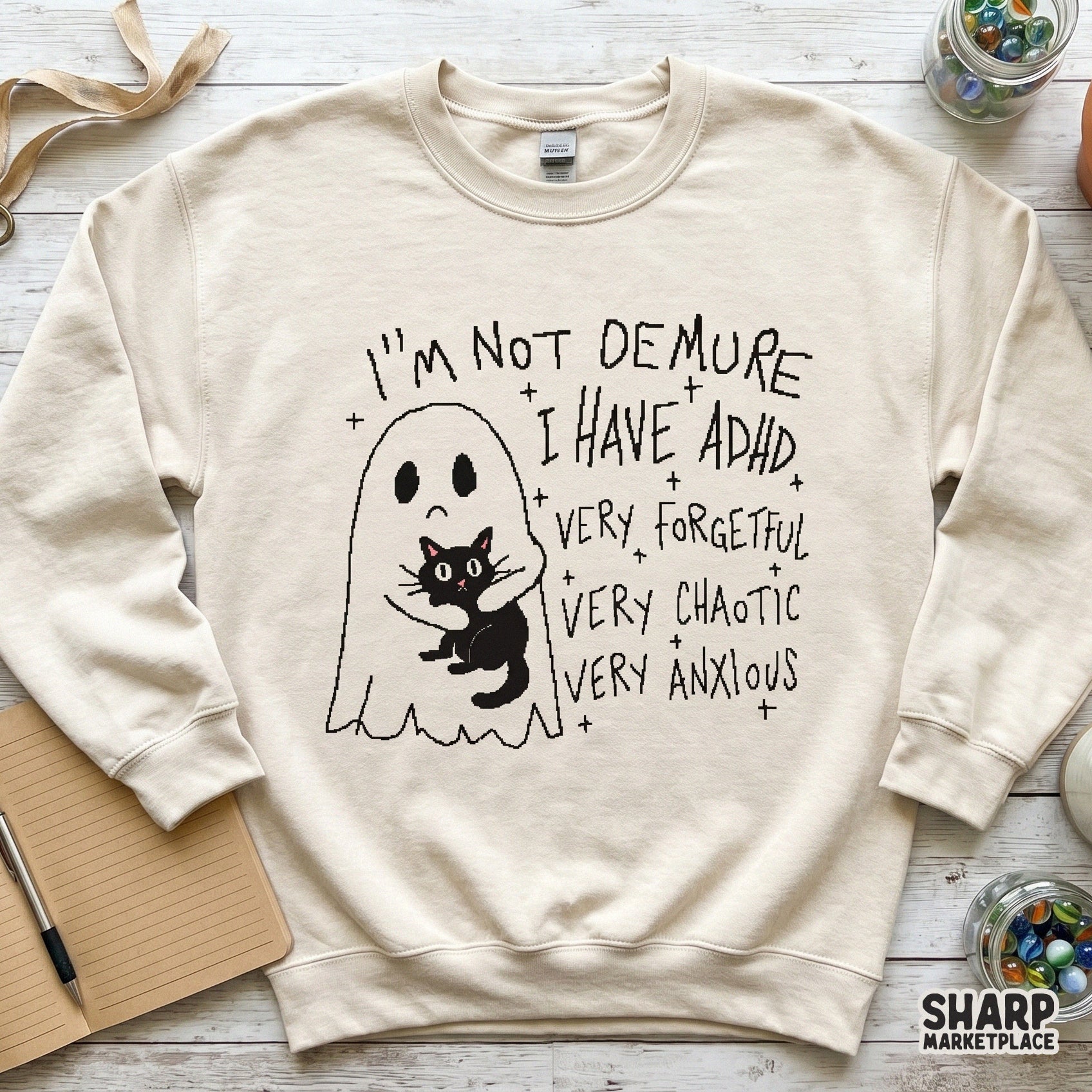 Digital design on a cream-colored sweatshirt featuring a ghost hugging a black cat with sarcastic ADHD text and star accents in a charcoal line art style.
