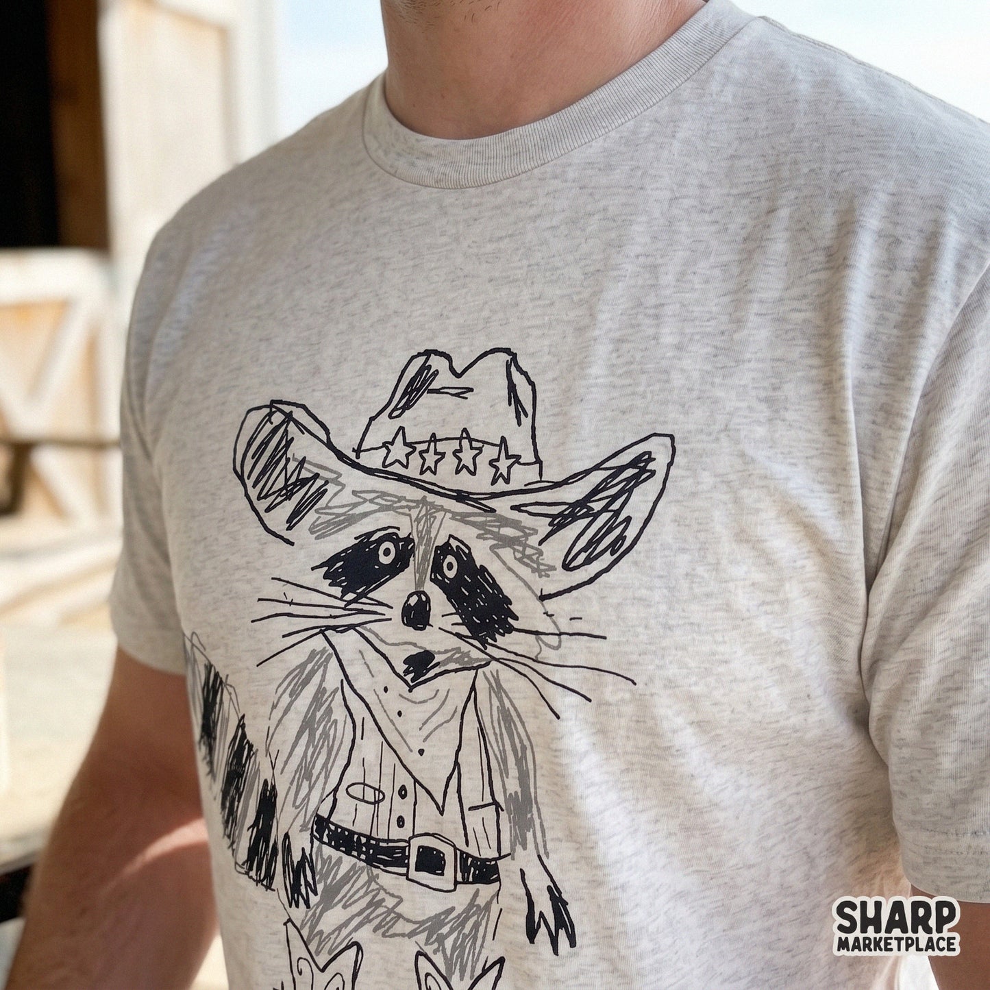 Close-up of a trendy retro-style raccoon cowpoke illustration printed on a heather gray t-shirt, ideal for custom country-themed clothing designs.