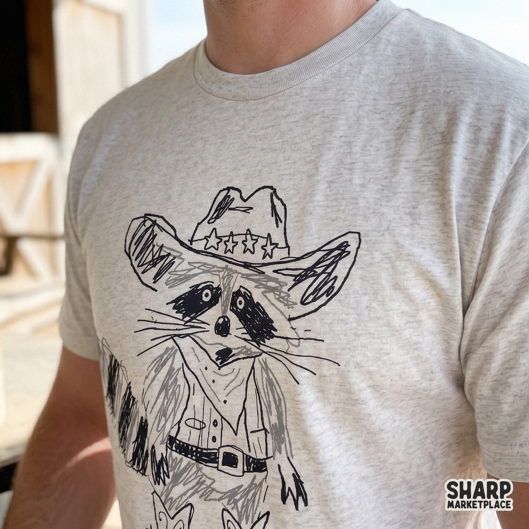 Close-up of a trendy retro-style raccoon cowpoke illustration printed on a heather gray t-shirt, ideal for custom country-themed clothing designs.