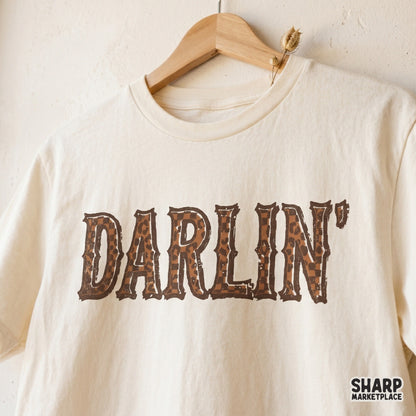 Western style Darlin graphic printed on a cream t-shirt, showcasing distressed brown leopard print lettering for a trendy southern cowgirl look.