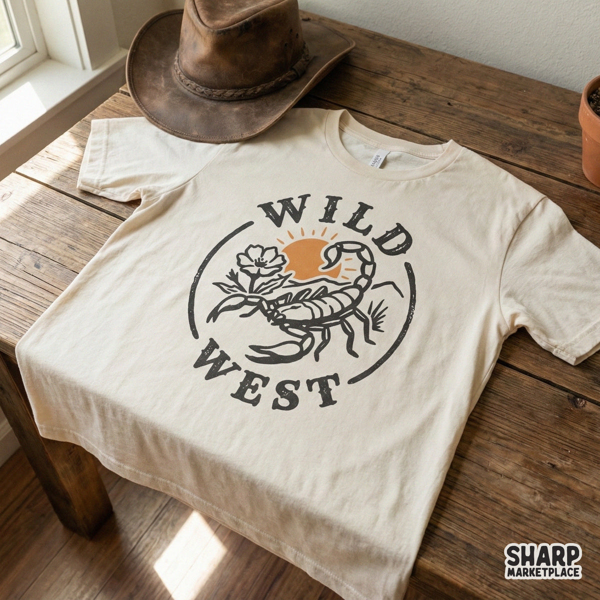 Western style graphic on a t-shirt mockup showing a scorpion and desert flower with Wild West text in a rustic, distressed circular design.