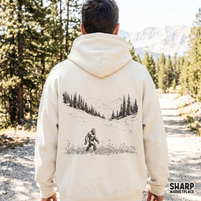 A beige hoodie featuring a detailed black line art illustration of a creature walking through a mountain meadow, perfect for outdoor apparel designs.