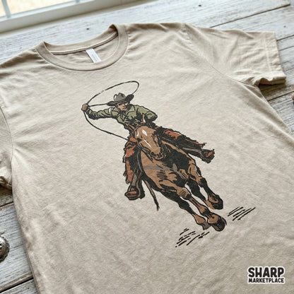 Detailed digital illustration of a rodeo rider on a galloping horse with a rope, presented on a beige t-shirt mockup for custom western clothing design.