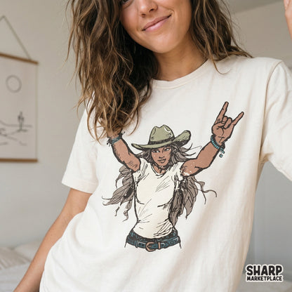 Trendy western cowgirl graphic featuring a woman in a cowboy hat and turquoise bracelets, shown printed on a cream-colored t-shirt for concert style.
