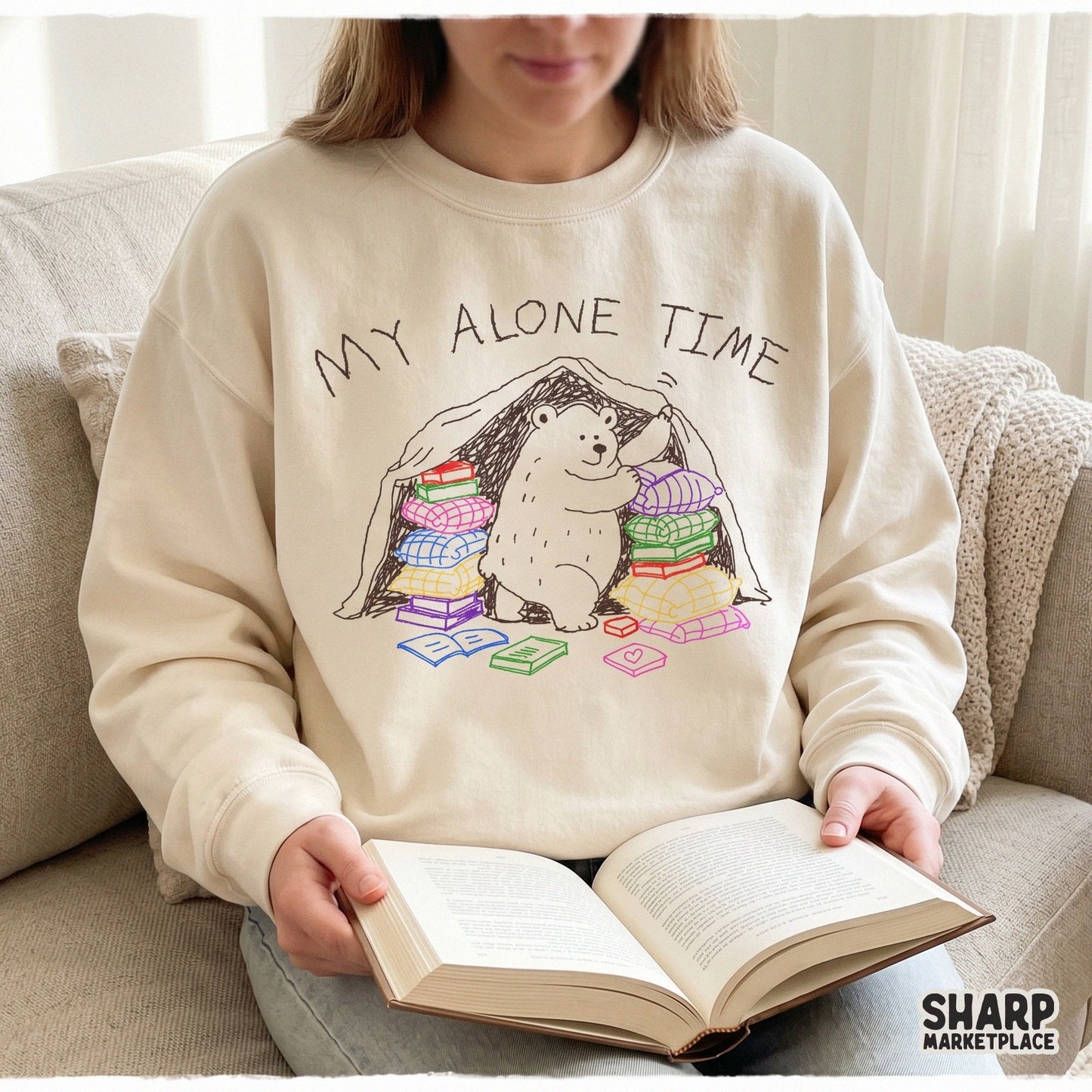 A cozy beige sweatshirt featuring a hand-drawn white bear inside a blanket fort with colorful books and the sarcastic quote My Alone Time Is For Everyone's