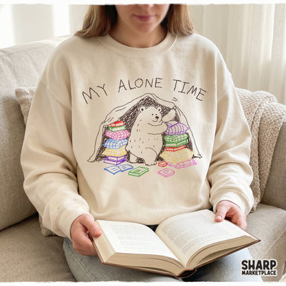 A cozy beige sweatshirt featuring a hand-drawn white bear inside a blanket fort with colorful books and the sarcastic quote My Alone Time Is For Everyone's