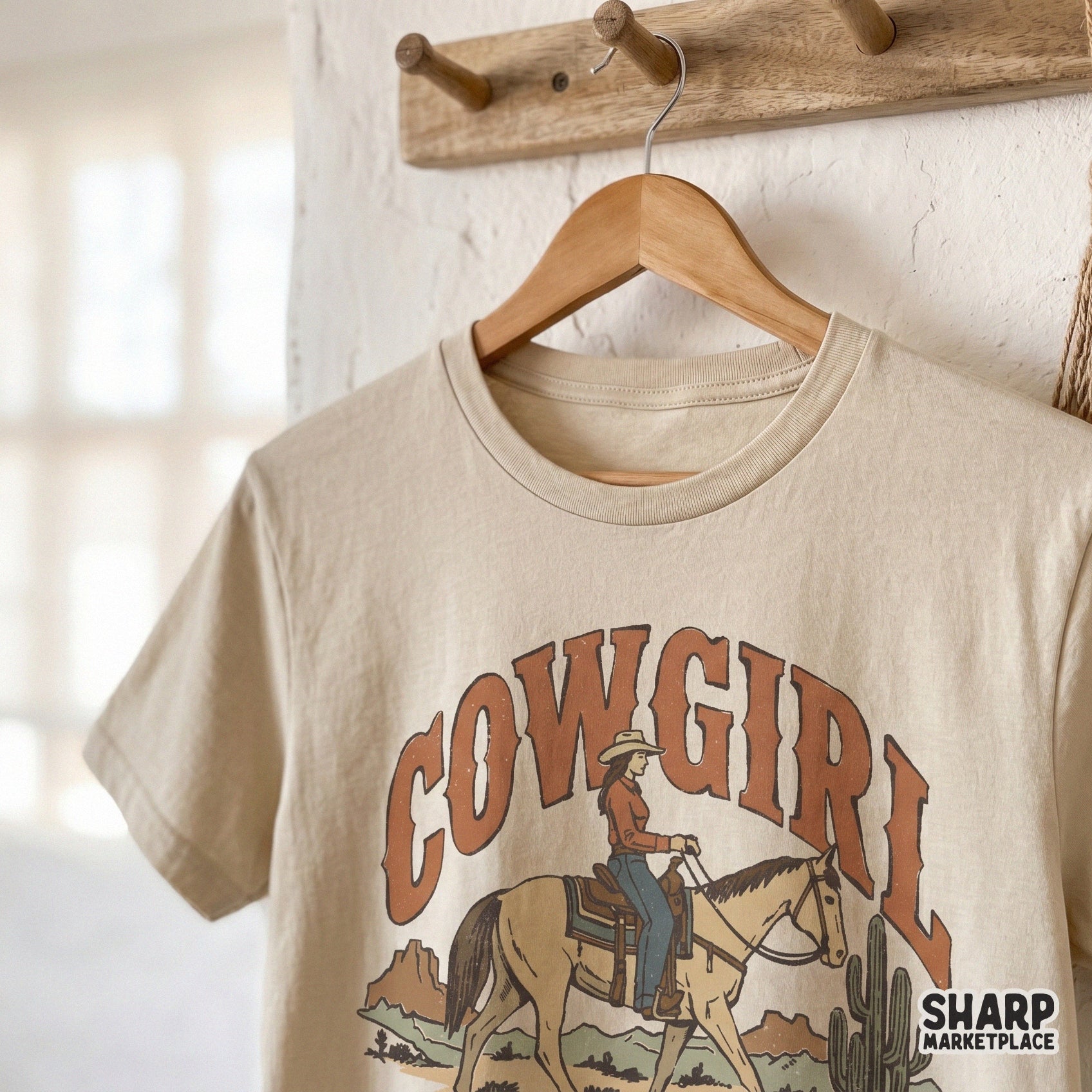 Vintage western sublimation design on a beige t-shirt mockup, showing a cowgirl on horseback with desert cactus art and retro arched text.