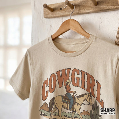 Vintage western sublimation design on a beige t-shirt mockup, showing a cowgirl on horseback with desert cactus art and retro arched text.