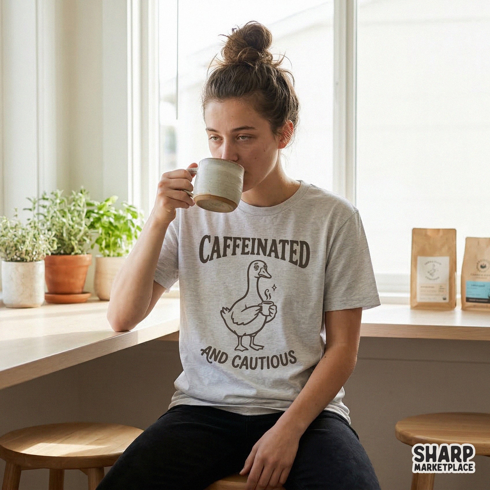 A light gray t-shirt featuring a funny cartoon duck holding a steaming cup of coffee with the arched text Caffeinated and Cautious in dark ink.