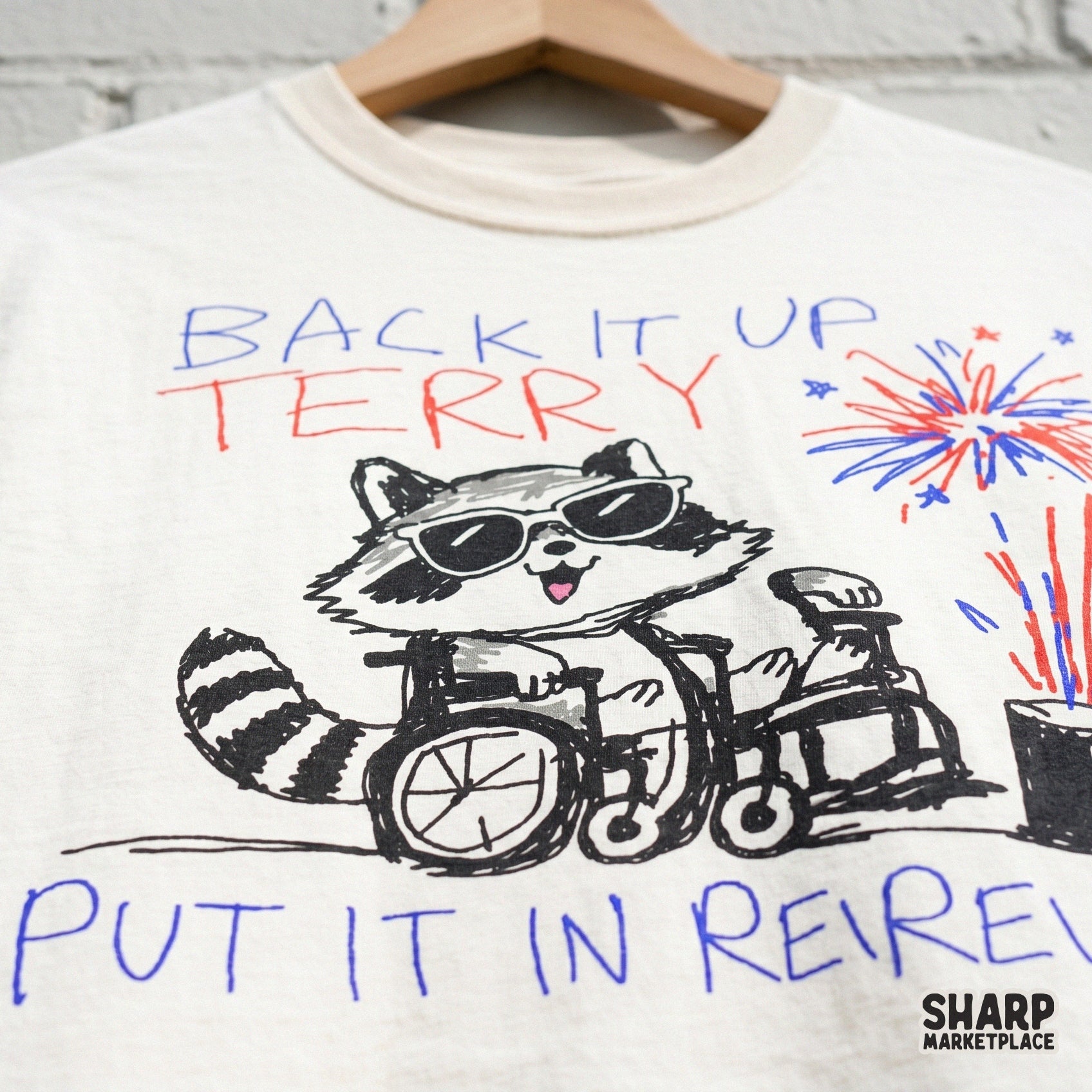 Funny raccoon in a wheelchair with red and blue fireworks and star accents, featuring the text Back It Up Terry Put It In Reverse for sublimation.
