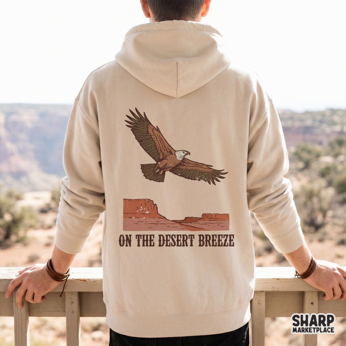 Beige hoodie mockup displaying a vintage southwest design of a soaring eagle over a red mesa canyon with the text On The Desert Breeze.