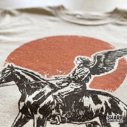 Close-up of a vintage-style winged rider on horseback illustration printed on a t-shirt, showcasing the distressed texture and sepia-toned artwork.
