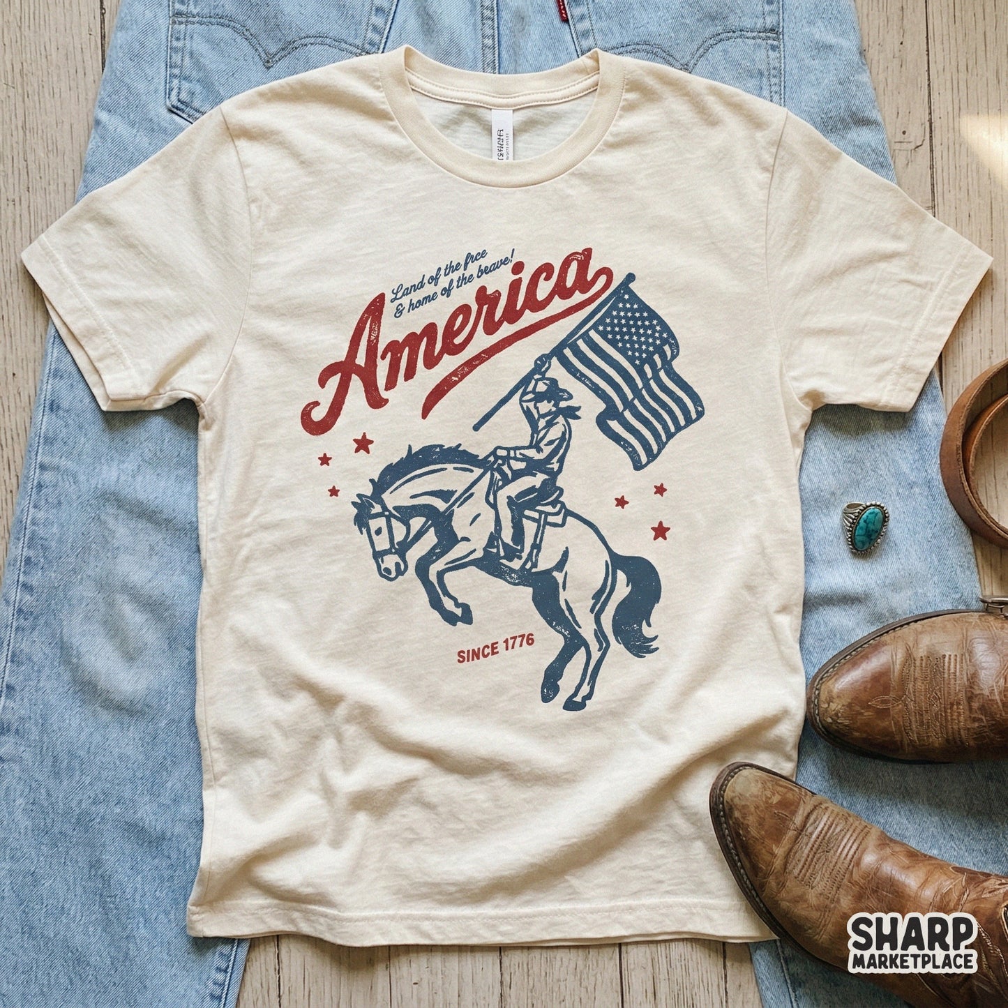 Distressed western style graphic printed on a cream t-shirt showing a cowboy riding a horse while waving a flag with the text America Since 1776.