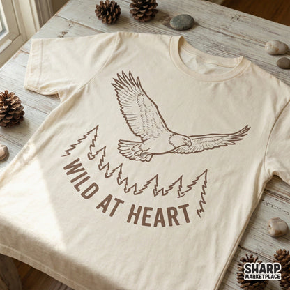A rustic brown eagle in flight over a forest scene with arched Wild At Heart text, featured as a digital graphic for custom t-shirts and sublimation.