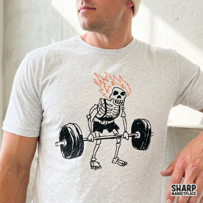 Funny gym ghoul graphic featuring a skeleton lifting weights with a fiery head, designed for custom t-shirts and sublimation transfers.