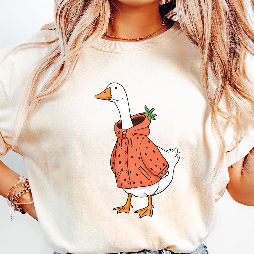 Trendy strawberry goose graphic on a cream-colored t-shirt, featuring a hand-drawn white goose in a fruit-themed raincoat.